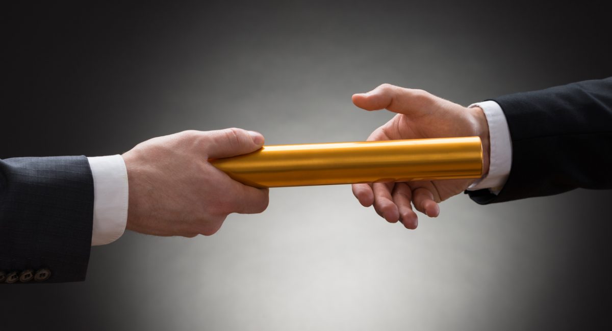 Close-up Of Two Businessman's Hand Passing A Golden Relay Baton